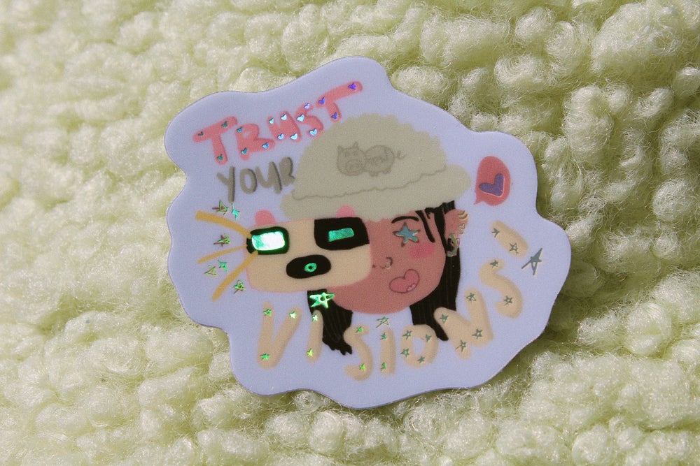 green fuzzy background with blue sticker in the middle. Sticker reads "Trust Your Visions!" in pink, green, and yellow text with holographic hearts and stars. The center image is a person with a green hat and a "TPN" pig holding a yellow camera and has a heart exclamation bubble.
