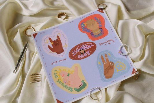 tan silk with rings around in the background. Blue sticker sheet with four hands stickers sits in the middle with a brown sticker reading Barkadababy in the middle.