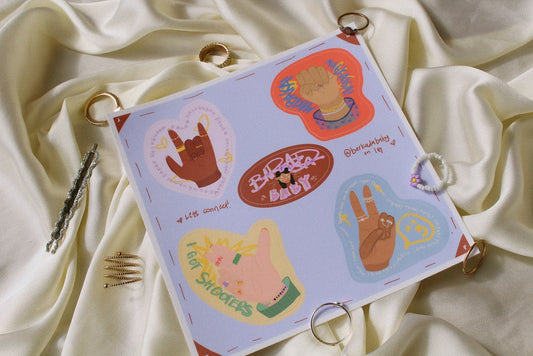 tan silk with rings around in the background.  Blue sticker sheet with four hands stickers sits in the middle with a brown sticker reading Barkadababy in the middle.