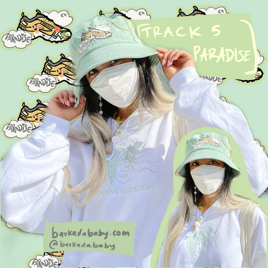 green background with track 5 paradise shoe sticker repeated in the background. there are green text boxes that read “[track 5 paradise]. barkadababy.com @barkadababy “ there is a collage of two photos of a masked person wearing a green corduroy bucket hat with gold chains attached”