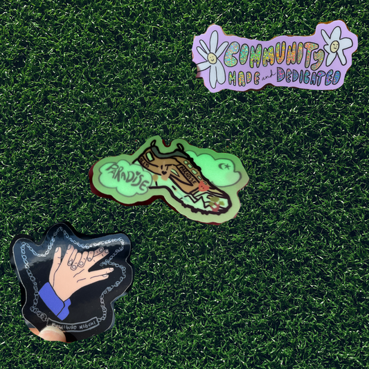fake grass background with picture of three individual stickers (megumi with blue background community made with a green background, and track 5 with a yellow) diagonal